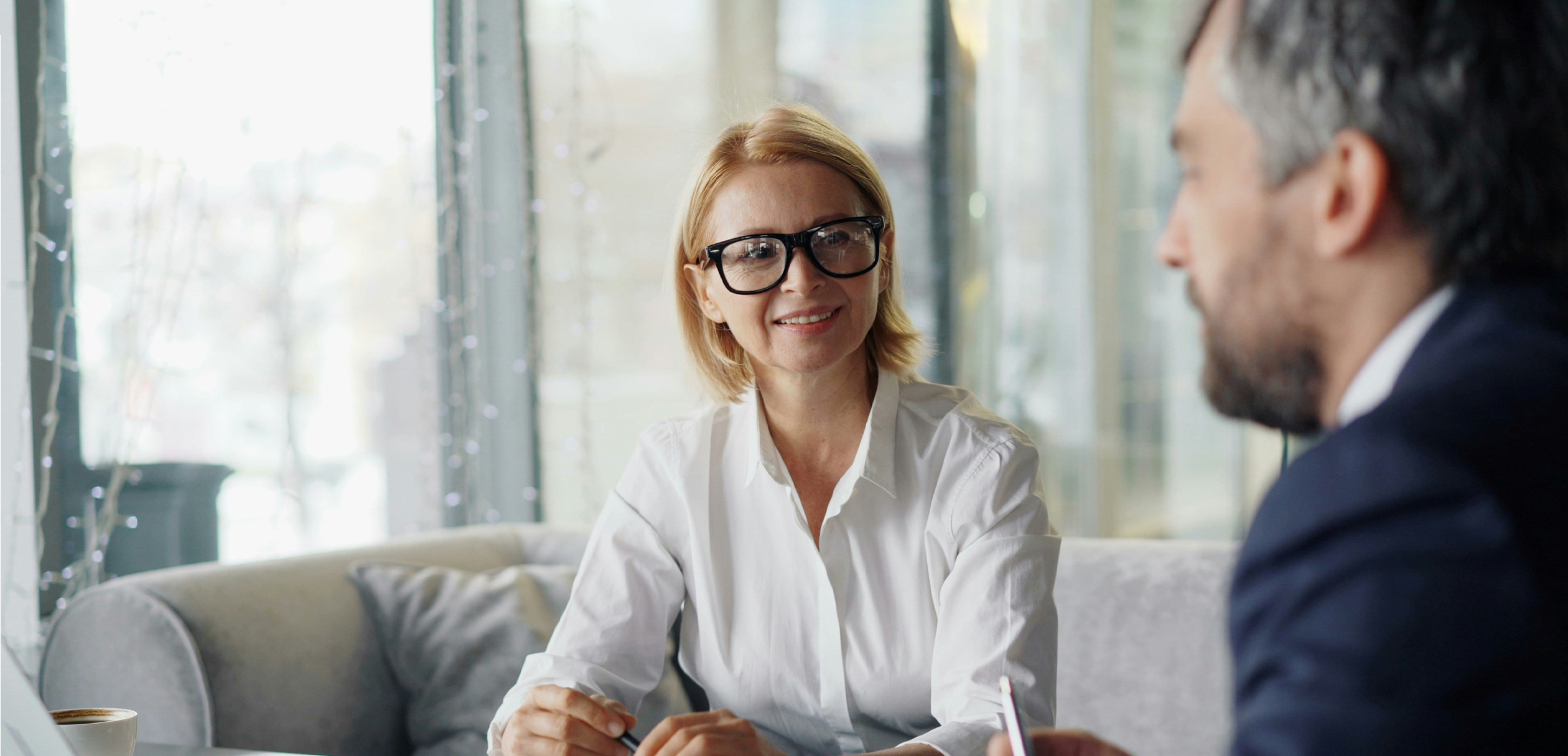 Woman in black glasses and white shirt speaking to a man blurred in the foreground